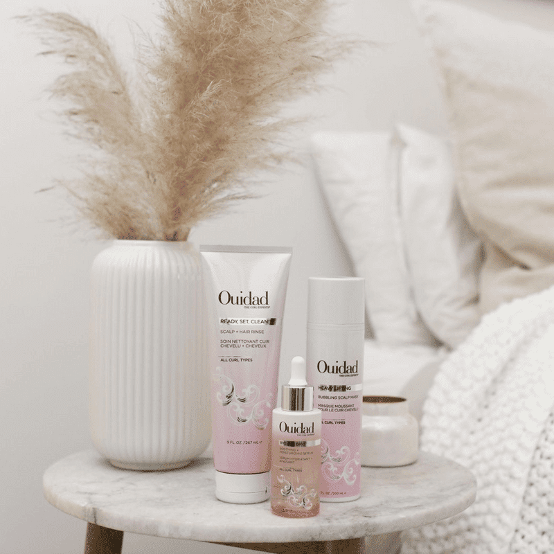 Hair care products on a marble table beside a vase with pampas grass.