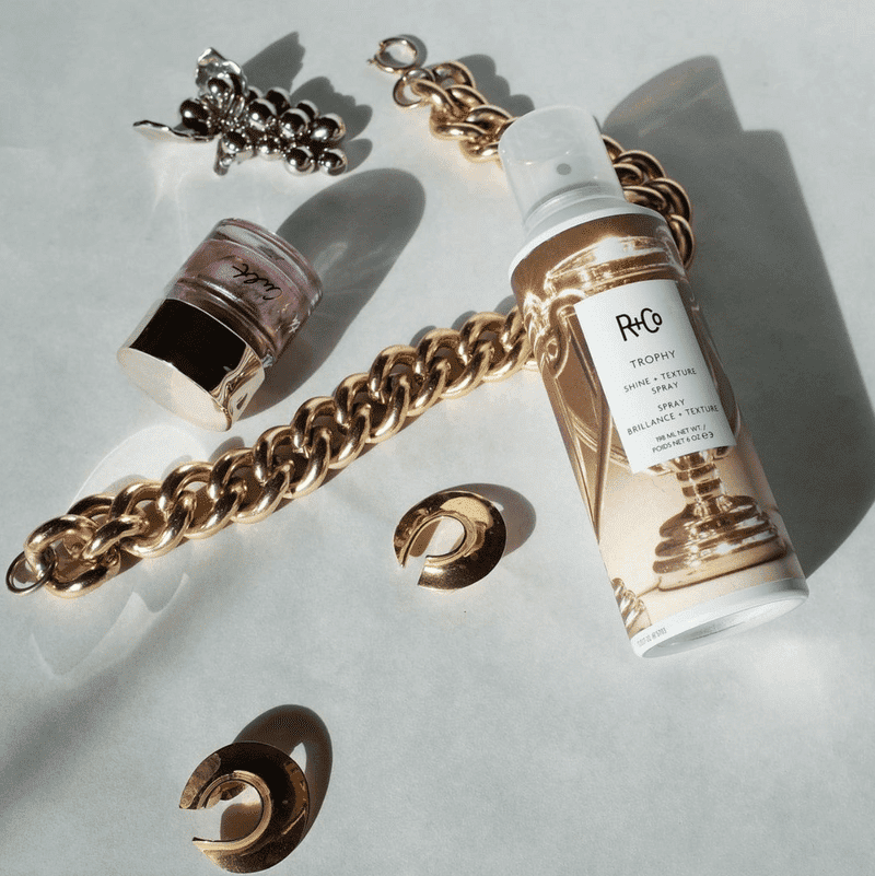 Styling spray, jewelry, and nail polish arranged on a white background.