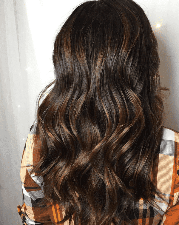 Wavy brown hair with highlights, styled in loose curls on a person wearing a plaid shirt.